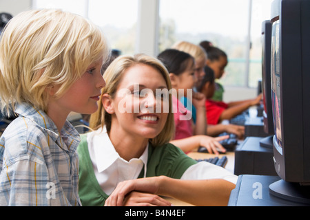 Docente aiutare lo studente a terminale di computer con gli studenti in background (profondità di campo/high key) Foto Stock