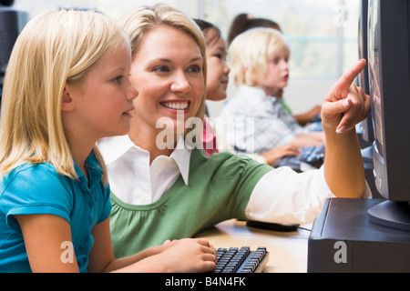 Docente aiutare lo studente a terminale di computer con gli studenti in background (profondità di campo/high key) Foto Stock