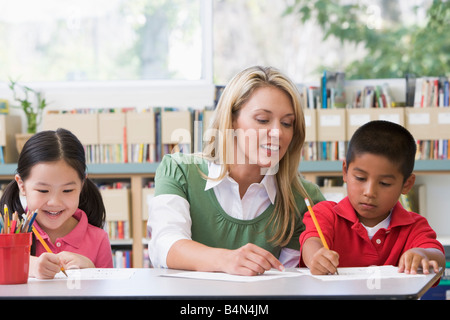 Due studenti in classe la scrittura con insegnante aiutando Foto Stock