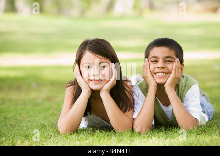 Due giovani bambini all'aperto giacente in park sorridente (messa a fuoco selettiva) Foto Stock