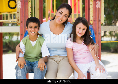 Madre e due giovani bambini seduti sulla struttura di gioco sorridente (messa a fuoco selettiva) Foto Stock