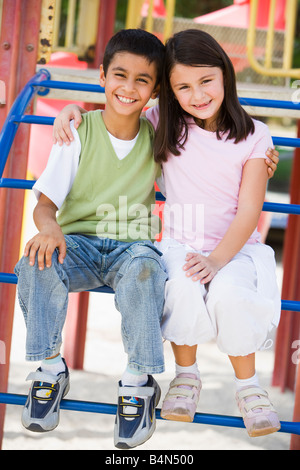 Due giovani bambini seduti sulla struttura di gioco sorridente (messa a fuoco selettiva) Foto Stock