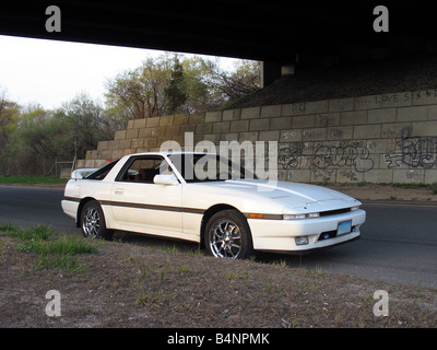 Un colpo di un bianco giapponese auto sportive al di sotto di una coperta di graffiti autostrada sopraelevata Foto Stock