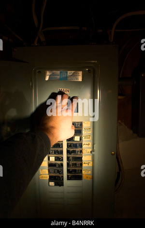 Una mano raggiunge per far scattare l'interruttore di circuito principale in una scatola interruttore illuminato con una luce flash. Foto Stock