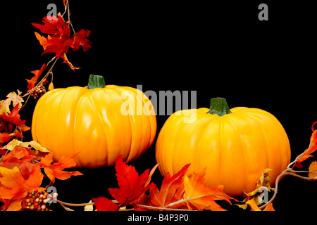 Due arancio brillante zucche disposta contro uno sfondo nero con alcune foglie di autunno a sinistra Foto Stock