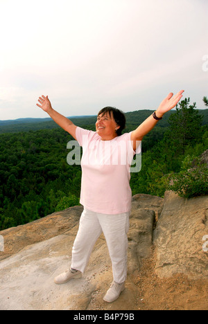 Donna matura in piedi su una scogliera i bracci di sollevamento nella gioia Foto Stock
