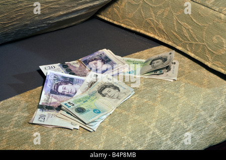 Risparmio di denaro diversi valori in sterline banca cassa note memorizzate in indoor nascondiglio per banconote sotto il divano divano cuscino sedia England Regno Unito Foto Stock