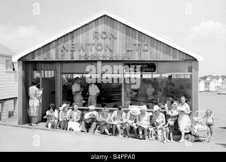 Vacanzieri godere il sole quanto essi siedono al di fuori di un negozio di scommesse in forma di chalet in legno sulla spiaggia a Dawlish Warren nel Devon Luglio 1962 Foto Stock
