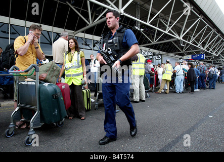 Poliziotti armati pattugliano le code di passeggeri in attesa al di fuori del Terminal 4 dell'aeroporto di Heathrow dove la British Airways ha annullato oltre il 40 percento dei suoi voli dopo il governo e le autorità aeroportuali hanno portato in più severe misure di sicurezza dopo l'interruzione di un complotto di bomba Agosto 2006 Foto Stock