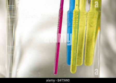 Close up sommerse e floating vivacemente colorato spazzolini da denti in vaso di vetro Foto Stock