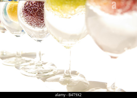 Una fila di bicchieri di vino contenente acqua frizzante e frutti vari in condizioni di luce intensa Foto Stock