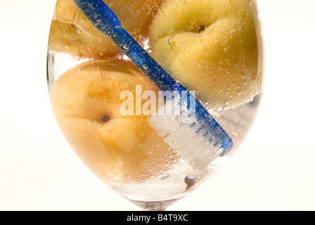 Close up di albicocche e spazzolino da denti blu immersi in un bicchiere da vino riempito con frizzanti acqua chiara Foto Stock