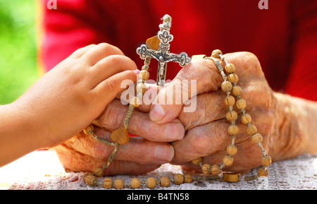 Bambino mani vecchia donna cattolica mano che trattiene il rosario Foto Stock
