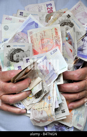 Pila di contanti composta di sterline assortite UK libbra banconote in valuta con mani che tengono denaro al petto di mans E tenuto afferrando le dita Inghilterra Foto Stock