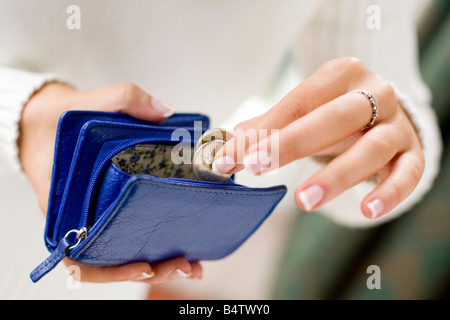 Giovane donna mettendo le monete in borsa Foto Stock