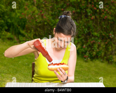Giovane donna versando il ketchup su hot dog Foto Stock