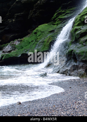 Cascata che scorre verso il basso nella scogliera sul mare e su una spiaggia di ciottoli. Foto Stock