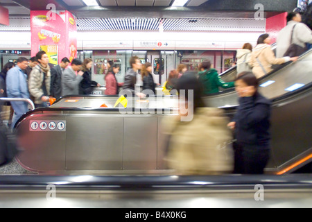 Un occupato di Tsim Sha Tsui sul MTR di Hong Kong con i pendolari che viaggiano sulle scale mobili con motion blur. Foto Stock