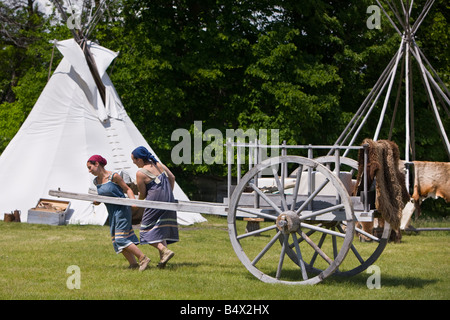 Interpreti in costume tirando un Fiume Rosso carrello con un teepee in background all'Accampamento Aborigeno di abbassare Fort Garry Foto Stock