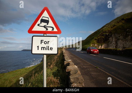 Automobile che viaggia oltre il fondo stradale sdrucciolevole pericolo rosso triangolo di avvertimento per 1 miglio segno sulla famosa A2 North Antrim causeway coastal Foto Stock