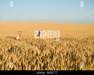 I bambini in esecuzione attraverso il frumento alto campo su wind farm Foto Stock