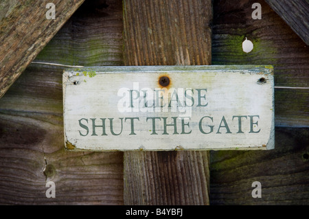 Cartello in legno su un giardino di lettura di gate si prega di chiudere il portone tenuto su da un chiodo arrugginito Foto Stock