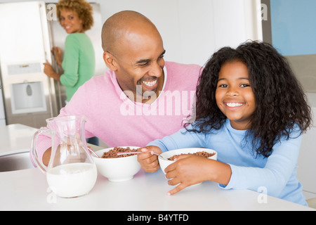 Padre seduto con la figlia come Lei essi mangiano colazione con sua madre in background Foto Stock