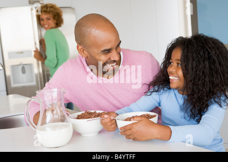 Padre seduto con la figlia come Lei essi mangiano colazione con sua madre in background Foto Stock