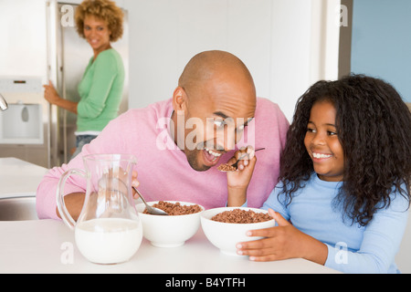 Padre seduto con la figlia come Lei essi mangiano colazione con sua madre in background Foto Stock