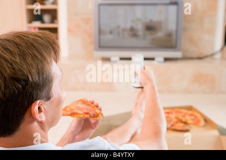 L'uomo godendo la Pizza mentre guardi la TV Foto Stock