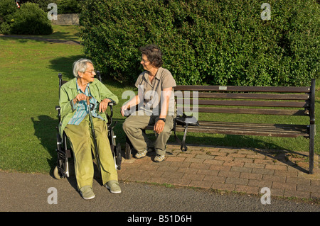 Medioevo donna con donna anziana in carrozzina seduta parlando in posizione di parcheggio Foto Stock
