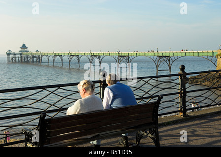 Anziana coppia seduta sul banco Clevedon lungomare affacciato sulla spiaggia e molo nord Somerset England Regno Unito Foto Stock