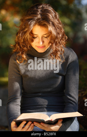 Giovane donna leggendo la Bibbia all'aperto vicino fino Foto Stock