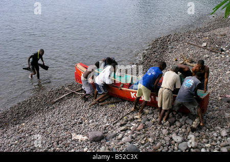 Pescatore tira nella loro barca in legno da Soufriere Bay sull'isola di Dominica. Foto Stock