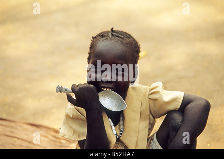 Una bella ragazza africana svolge con un cucchiaio vicino alla sua casa nel suo villaggio Foto Stock