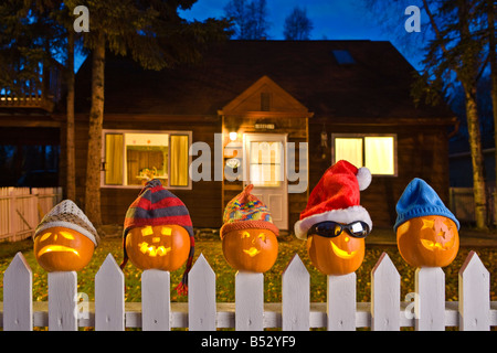 Jack-O-Lantern facce calza da indossare tappi, bloccata in posizione sulla sommità del bianco picktet recinzione al crepuscolo caduta Anchorage in Alaska,. Foto Stock