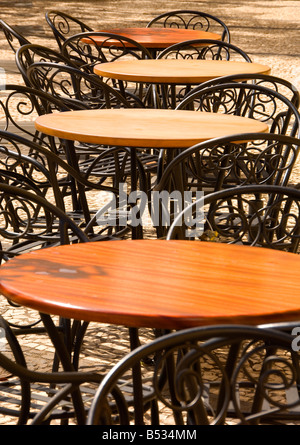 Al di fuori di cafe con vuoto in legno circolare sormontato i tavoli e le sedie in acciaio in una riga Foto Stock