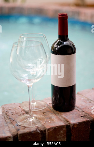 Un vino rosso bottiglia e due bicchieri vuoti dal pool abbondanza di spazio copia sul vuoto etichetta del vino Foto Stock