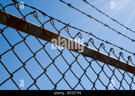 Recinzione barbwire contro il cielo blu con i raggi del sole Foto Stock