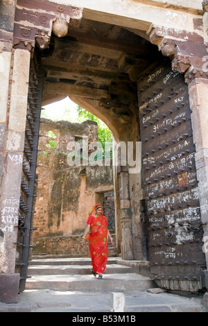 Una donna indiana in un sari rosso passeggiate attraverso un cancello in Ranthambore fort, il Parco nazionale di Ranthambore, Rajasthan, India Foto Stock