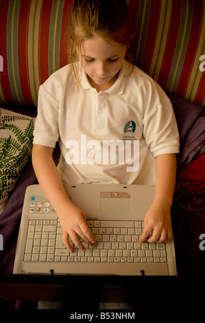 Dieci anni di scuola primaria bambino utilizzando laptop computer facendo tappa chiave 2 compiti a casa seduti sul divano nel soggiorno di casa, REGNO UNITO Foto Stock