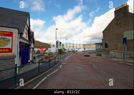 Car driving along road passing a green light in Fort William Scotland UK with Loch and hills behind Foto Stock