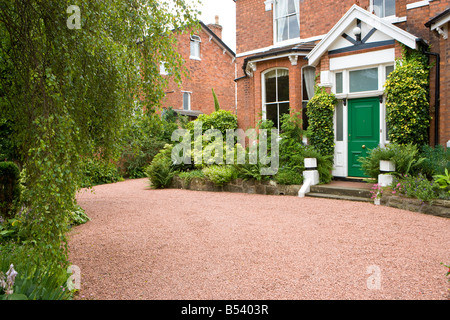 Giardino frontale di una grande casa unifamiliare con red stradina di ghiaia e holly boccole Foto Stock