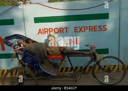 New Delhi rickshaw driver dorme nella parte anteriore della parete di un edificio sito dicendo la linea Airport Express. Foto Stock