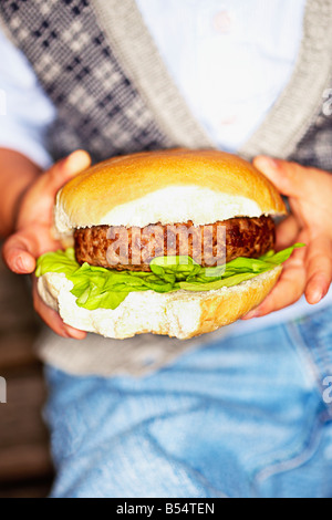 Close-up di Little Boy tenendo un hamburger di manzo nelle sue mani Foto Stock