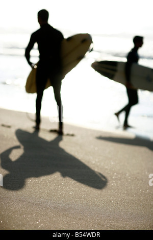 Le ombre dei due surfers può essere visto sulla sabbia come si cammina su una spiaggia al tramonto a Colares vicino a Lisbona in Portogallo Foto Stock