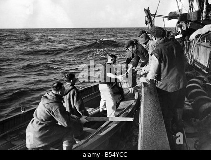 La flotta di pesca aiuta il Navy.. Questi Peschereccio gli uomini credono che una buona volta merita un altro e qui nel Mare del Nord sono visto passare un paio di ceste di pesce per alcuni di un equipaggio di un dragamine britanniche (in piccola barca) che ha appena lasciato minesweeper in background. Basta un po' di apprezzamento per gli uomini che per spazzare via le mine vaganti ecc nel Mare del Nord e a rendere più sicura la pesca. Novembre 1942 P012252 Foto Stock