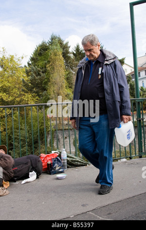 L'uomo sul modo di compilare l'acqua santa, ma ignorando i senzatetto uomo sulla strada - Lourdes, Francia meridionale Foto Stock