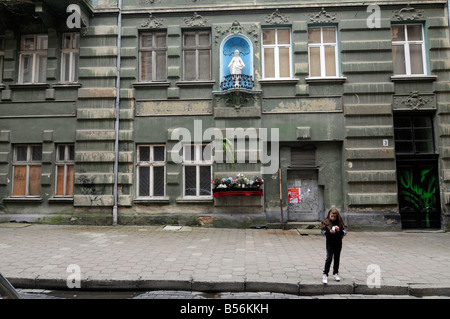 Scena di strada in Lvov, Ucraina. Una giovane ragazza cammina davanti a un edificio con un piccolo altare per la Vergine Maria. Foto Stock