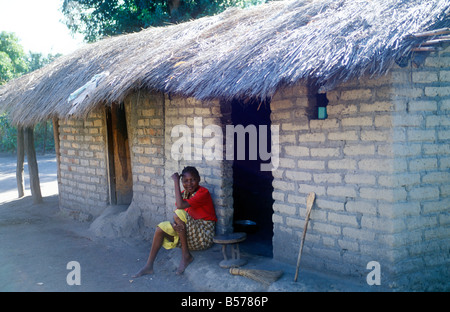 Una donna seduta accanto alla sua casa di paglia in un villaggio vicino a Spiaggia di Kande, il Lago Malawi, Africa Foto Stock